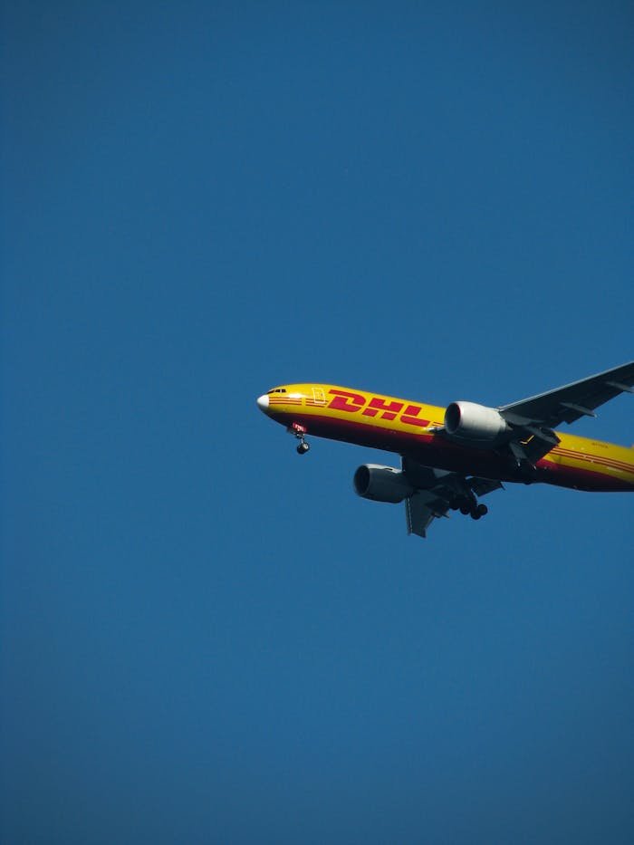 services-03 A DHL cargo plane flying against a clear blue sky during the day. Ideal for aviation and logistics themes.